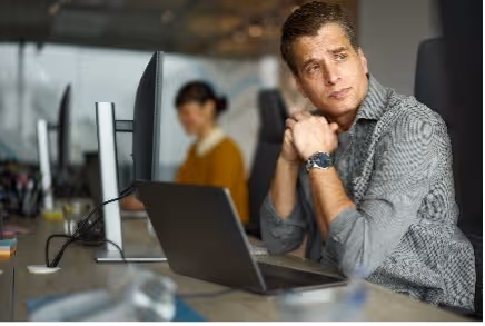 Man kijkt peinzend opzij terwijl hij achter een laptop op kantoor zit.