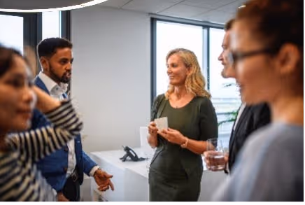 Groep collega’s praat informeel bij het raam, terwijl een vrouw een mok vasthoudt.