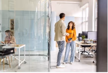 Man en vrouw staan tegenover elkaar te praten in een modern kantoor met glazen wanden.