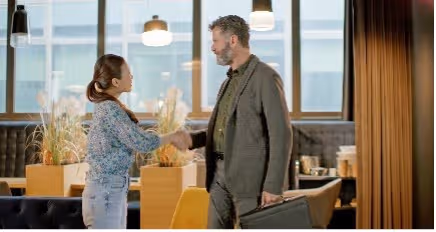 Man en vrouw schudden elkaar de hand in een moderne kantoorruimte met grote ramen.
