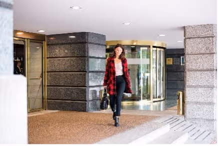 Vrouw in een rood-zwart geruite jas loopt een gebouw uit via een draaideur.