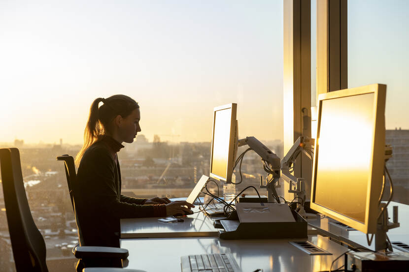 Vrouw achter laptop met zonsondergang op achtergrond
